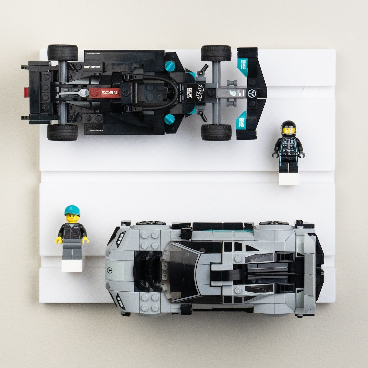 Two detailed racing car models and two mini-figures are presented on a three-tiered white shelf, with the cars spanning the top two tiers.